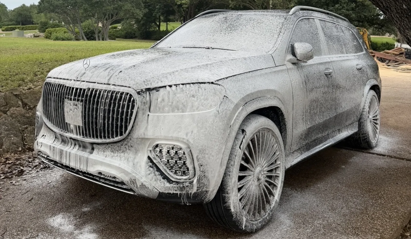 Mercedes-Maybach SUV covered in thick white wash foam on a driveway under an oak tree