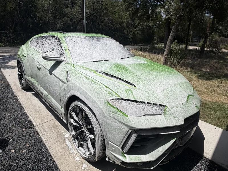 Lamborghini SUV covered in thick white wash foam on a driveway during an exterior hand wash